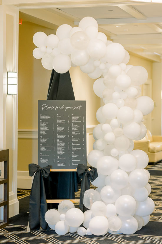 Black and white wedding reception seating chart with balloon arch