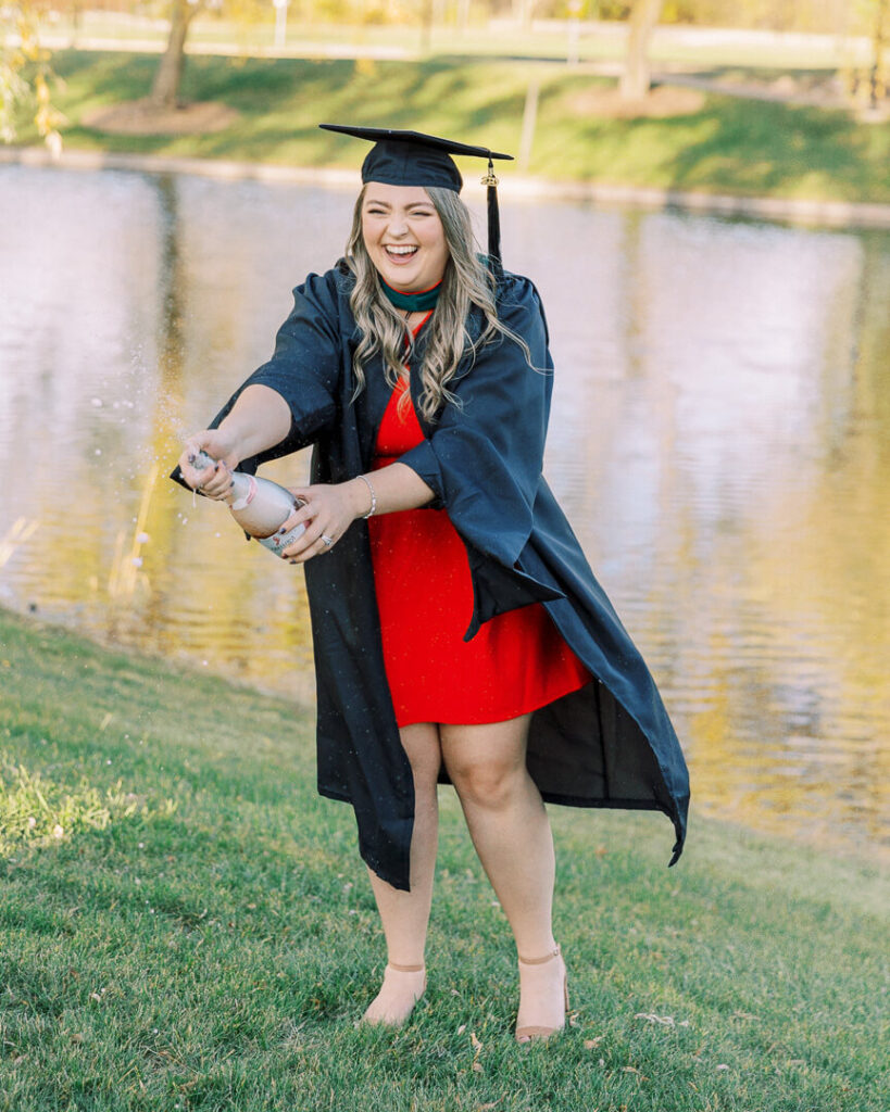 Saginaw Valley State graduates in cap and gown popping champagne in red dress
