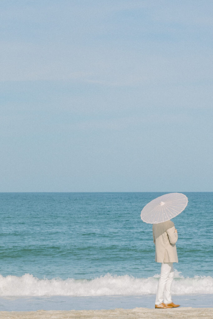 groom in tan suit with paper parasol beach wedding1